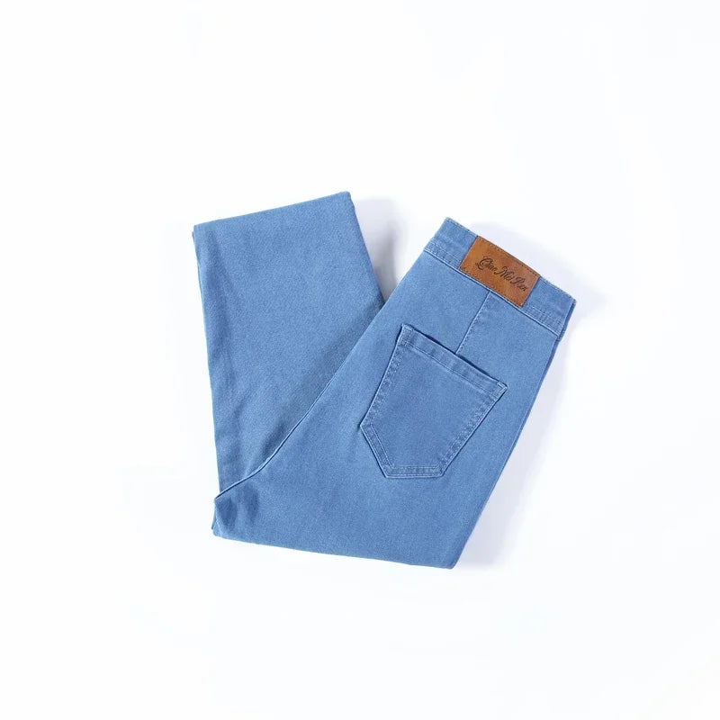 A pair of Cotton Elastic Denim Jeans in light blue, featuring a mid-waist fit, button fly closure, and sash and button decorations. These full-length pencil pants offer high stretch fabric for comfort and style, perfect for all occasions.