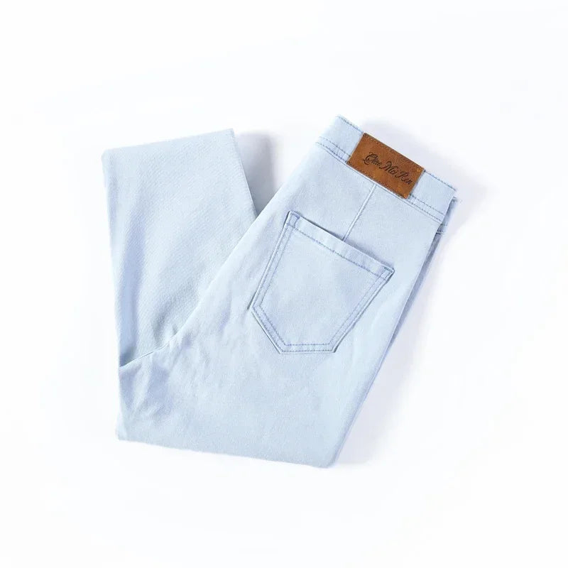 A pair of Cotton Elastic Denim Jeans in light blue, featuring a mid-waist fit, button fly closure, and sash and button decorations. These full-length pencil pants offer high stretch fabric for comfort and style, perfect for all occasions.