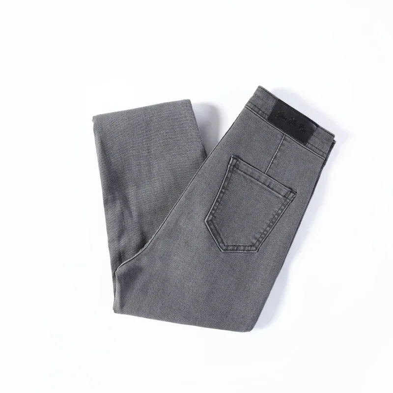A pair of Cotton Elastic Denim Jeans in light blue, featuring a mid-waist fit, button fly closure, and sash and button decorations. These full-length pencil pants offer high stretch fabric for comfort and style, perfect for all occasions.