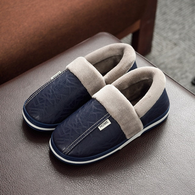 A pair of men's indoor slippers made of proportioned PU and plush insole material. The slippers are a light brown color and have a comfortable, relaxed design.