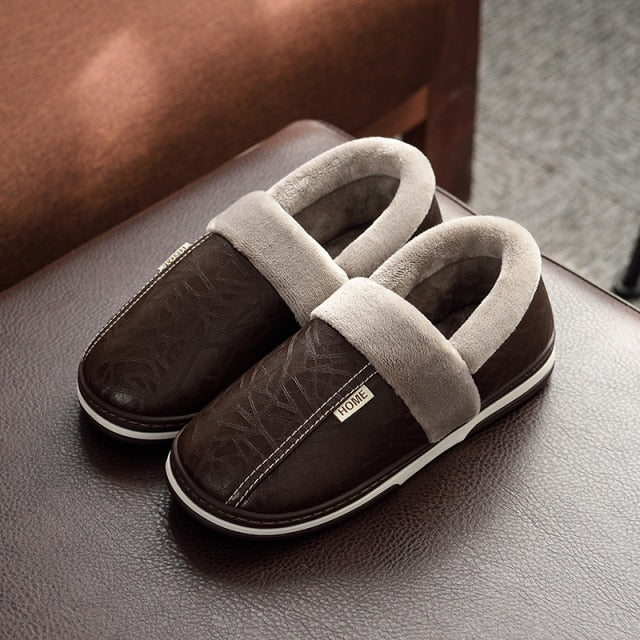 A pair of men's indoor slippers made of proportioned PU and plush insole material. The slippers are a light brown color and have a comfortable, relaxed design.